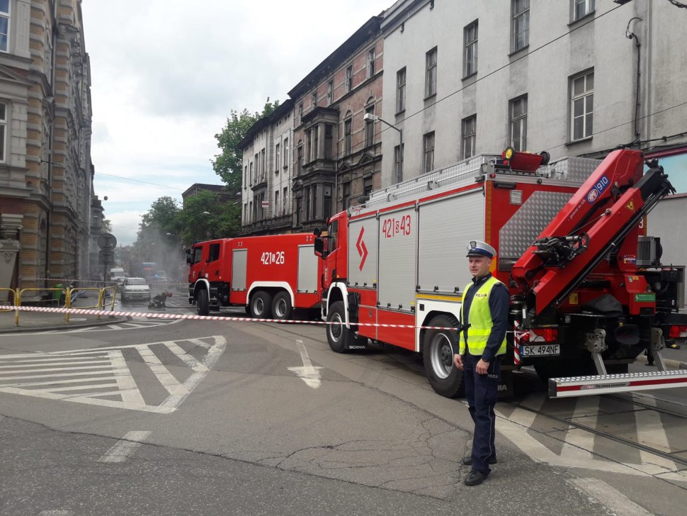 ul Powstańców w Chorzowie, na pierwszym planie widoczny policjant  z Wydziału Drogowego kierujący ruchem,  w tle widoczne dwa wozy bojowe straży pożarnej oraz strażacy.