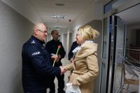 Na pierwszym planie widoczny jest pierwszy Zastępca Komendanta Miejskiego Policji w Chorzowie wręczający kwiaty kobiecie wchodzącej do Komendy Miejskiej Policji , na drugim planie widoczny jest Naczelnik Wydziału Ruchu Drogowego oraz Naczelnik Wydziału Sztab Policji