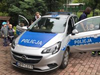 dzieci w asyście umundurowanej policjantki oraz przedszkolanki oglądają radiowóz oznakowany