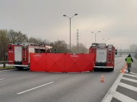 Wozy strażackie na miejscu wypadku pomiędzy nimi rozwinięty parawan obok idący policjant