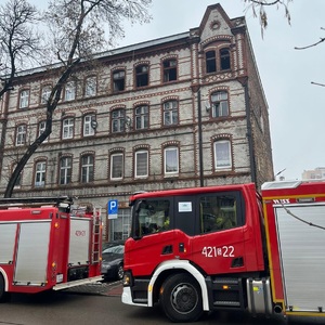 Zdjęcie przedstawia pojazdy straży pożarnej, w tle kamienica w której wybuchł pożar.