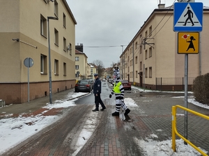 Zdjęcie przedstawia policjanta drogówki oraz maskotkę straży miejskiej przechodzących przez przejście dla pieszych