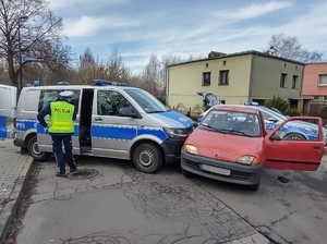 Zdjęcie przedstawia pojazd uciekinierów, policjanta drogówki oraz dwa policyjne radiowozy.