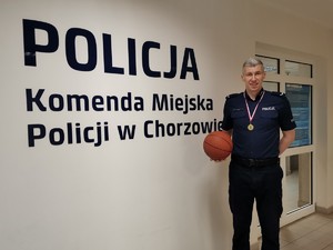 Zdjęcie przedstawia naszego policjanta z medalem oraz piłką do koszykówki