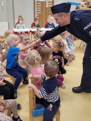 Zdjęcie przedstawia grupę dzieci oraz policjanta witającego się z jednym z nich