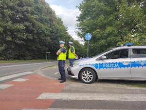 Zdjęcie przedstawia policjantów nadzorujących ruch kołowo oraz policyjny radiowóz