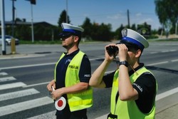 Zdjęcie przedstawia dwóch policjantów drogówki. Jeden z nich patrzy przez lornetkę