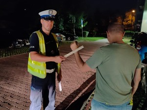 Zdjęcie przedstawia policjanta wręczającego odblaskową opaskę pieszemu