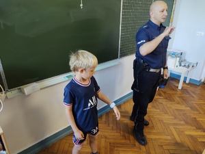 Zdjęcie przedstawia policjanta oraz jednego z uczniów podczas zakładania elementu odblaskowego.