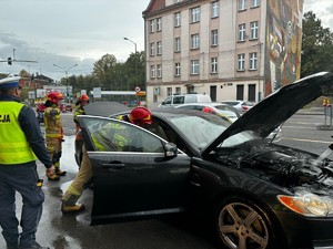 Zdjęcie przedstawia policjanta i strażaków podczas gaszenia palącego się samochodu