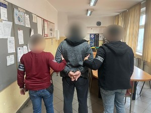 Zdjęcie przedstawia zatrzymanego mężczyznę asekurującego go przez dwóch nieumundurowanych policjantów