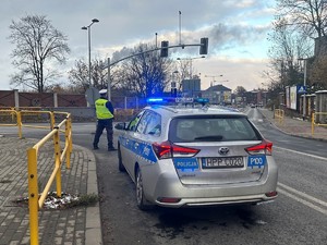 Zdjęcie przedstawia policjanta kierującego ruchem oraz radiowóz