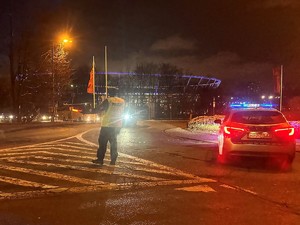 Zdjęcie przedstawia policjanta kierującego ruchem podczas opuszczania stadionu przez kibiców