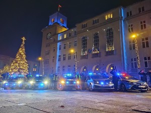 Zdjęcie przedstawia policjantów oddających honor stojących obok radiowozów