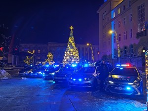 Zdjęcie przedstawia policjantów oddających honor stojących obok radiowozów