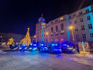 Zdjęcie przedstawia policjantów oddających honor stojących obok radiowozów