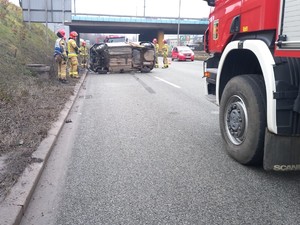 Zdjęcie przedstawia pojazd straży pożarnej podczas próby postawienia pojazdu osobowego z dachu na koła