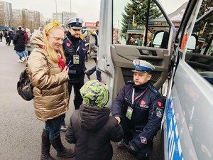 Zdjęcie przedstawia rodzica z dzieckiem przy radiowozie oraz policjantów