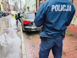 Zdjęcie przedstawia policjanta i nieprawidłowo zaparkowany pojazd.