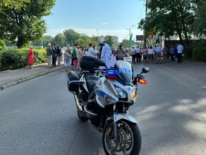 Zdjęcie przedstawia policyjny motocykl na tle procesji