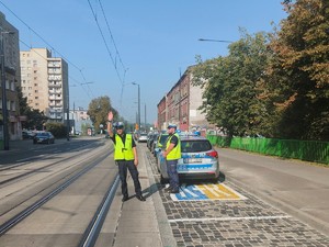 Zdjęcie przedstawia policjanta zatrzymującego do kontroli samochód w rejonie szkoły