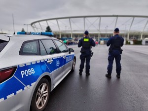 Zdjęcie przedstawia radiowóz oraz policjantów na tle stadionu