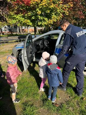 Zdjęcie przedstawia policjanta oraz dzieci podczas oglądania radiowozu