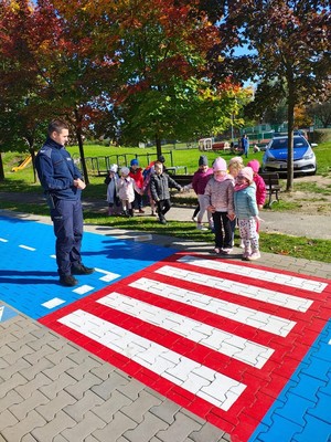 Zdjęcie przedstawia policjanta oraz dzieci podczas przechodzenia przez przejście dla pieszych