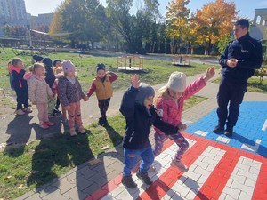 Zdjęcie przedstawia policjanta oraz dzieci przy przechodzeniu przez przejście dla pieszych