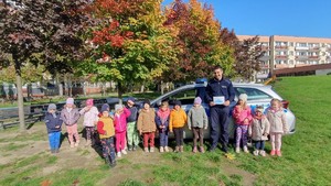 Grupowe zdjęcie dzieci i policjanta na tle radiowozu