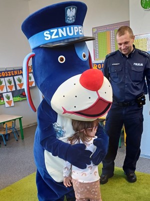 Na zdjęciu Sznupek przytulający dziecko oraz policjant.