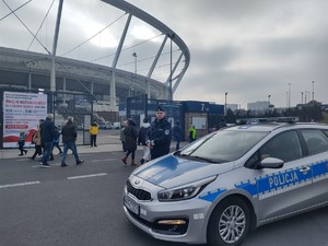 Na zdjęciu policjant przy radiowozie na tle stadionu.