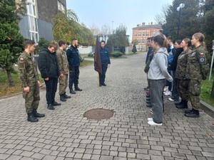 Zdjęcie na zewnątrz szkoły. Dwójka policjantów i uczniowie szkoły.