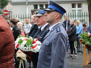Na zdjęciu oficerowie służb mundurowych  z kwiatami w kolorze biało czerwonym. Źródło: naszemiasto.pl