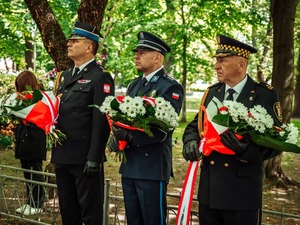 Na zdjęciu trzej przedstawiciele służb mundurowych z kwiatami w rękach .