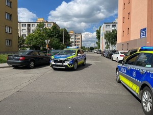 Na zdjęciu widać  bloki, ulicę, dwa radiowozy oraz samochody.