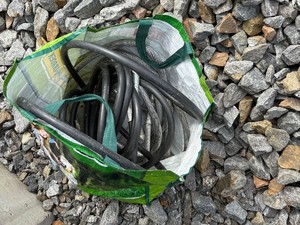 Na zdjęciu czarne kable w zielonej torbie ułożonej na kamieniach