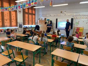 Na zdjęciu policjant i policjanta w czasie prelekcji oraz dzieci siedzące w ławkach szkolnych w klasie