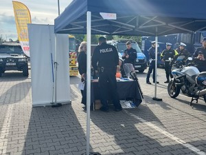Na zdjęciu policjanci w trakcie pikniku bezpieczeństwa pod namiotem na tle samochodów służbowych