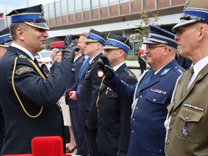 Na zdjęciu oficerowie służb mundurowych składający sobie honor  na tle wiaduktu