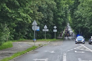 Na zdjęciu widoczny z daleka jadący radiowóz a za nim rowerzyści