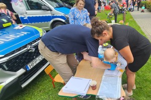 Na zdjęciu kobieta z dzieckiem na rękach pochylona nad stolikiem oraz mężczyzna
