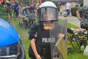 Na zdjęciu dziecko w białym kasku w kamizelce kuloodpornej i tarczą policyjną