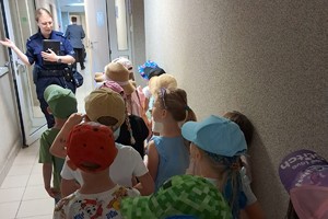 Na zdjęciu grupa dzieci w Komendzie Miejskiej Policji w Chorzowie i policjanta stojąca przed nimi, skierowana do nich przodem.