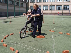 Na zdjęciu policjantka trzymająca rower, na którym siedzi dziecko