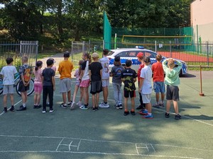 Na zdjęciu grupa dzieci na boisku szkolnym patrząca na radiowóz