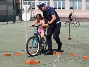 Na zdjęciu policjant trzymający rower, na którym siedzi dziecko