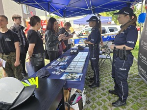 Na zdjęciu dwie policjantki stojące za stołem z materiałami promocyjnymi policji i grupa ludzi przed nimi