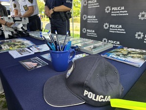 Na zdjęciu czapka policyjna, granatowy kubek z ołówkami i materiały promocyjne policji leżące na stole