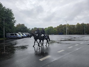 Na zdjęciu radiowozy policyjne oraz dwaj policjanci na koniach służbowych